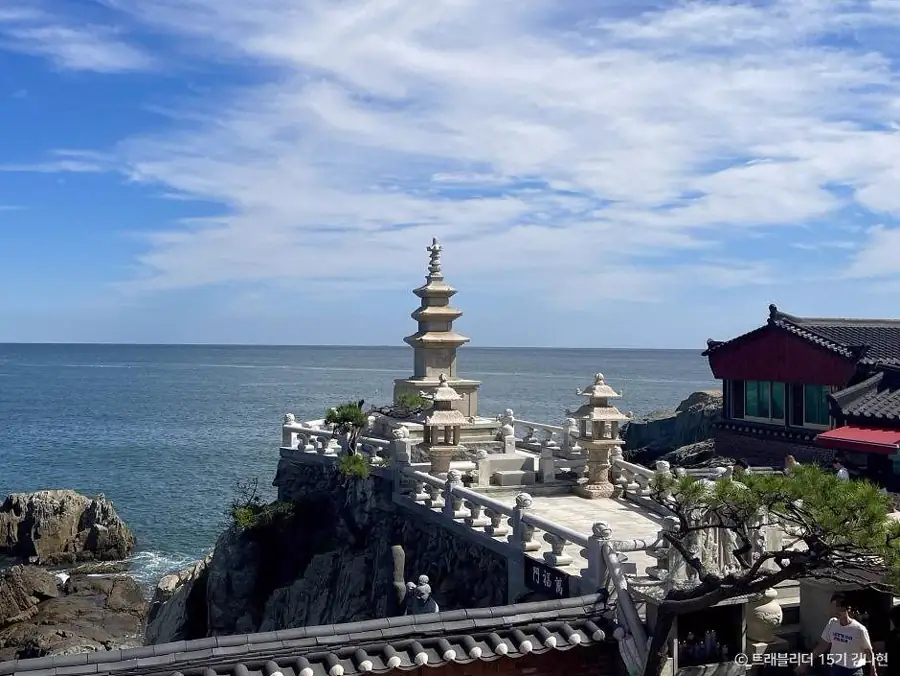 A white stone pagoda beside the sea at Haedong Yonggungsa, with a tiled temple hall and open horizon