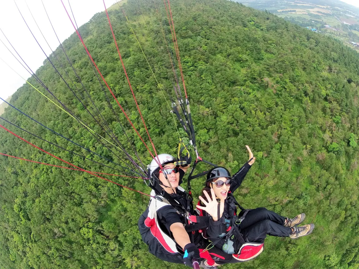 Tandem paragliding flight above Jeju oreum and fields