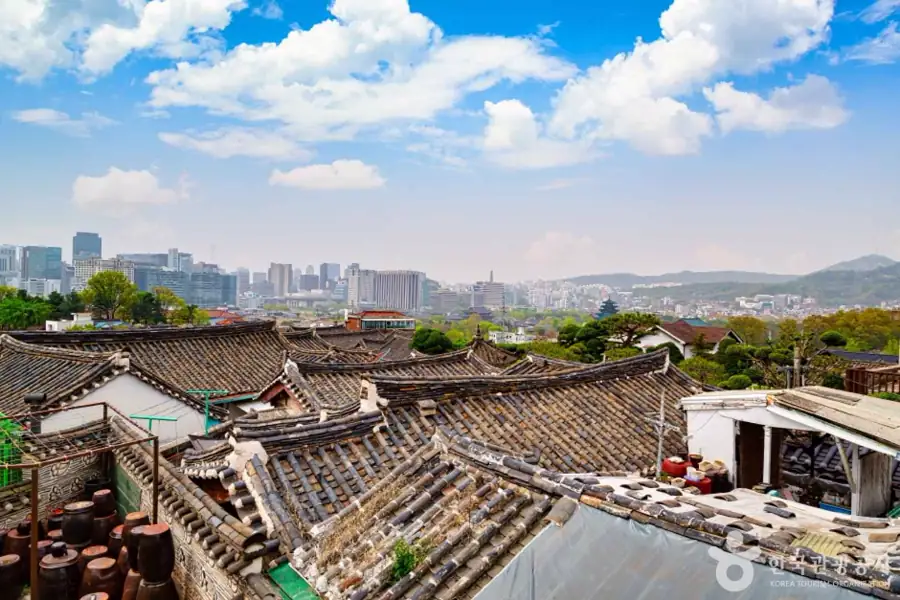 Hanok rooftops in Bukchon with modern Seoul buildings in the distance.